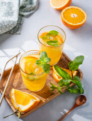 Freshly squeezed juice in a glass with fresh oranges, mint and ice on a light background with metallic tube and shadow. Healthy citrus detox drink for breakfast.