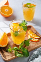 Freshly squeezed juice in a glass with fresh oranges, mint and ice on a light background with metallic tube and shadow.