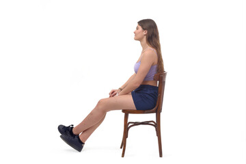 side view of a young girl sitting on chair stretched legs on white background