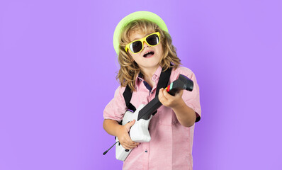 Portrait of little boy in pink sunglasses playing electric guitar. Cute child boy sings and plays on the electric guitar with bright emotions.