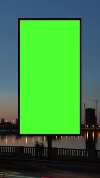 Timelapse green screen billboard on waterfront with night traffic. Vertical lightbox with chroma key on city street. Streetlights reflection on water. Commercial information and Generative AI