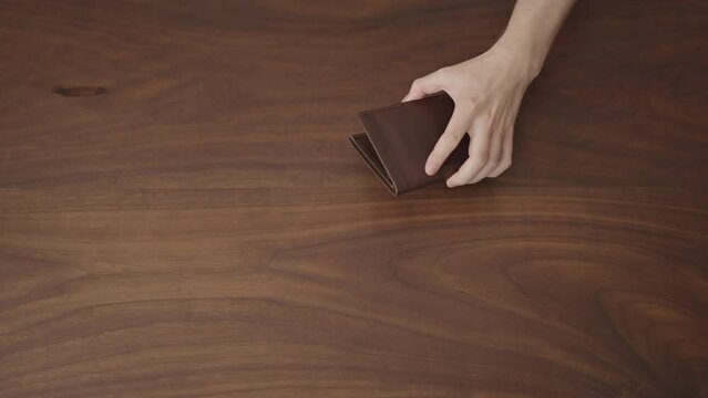 Man put money in leather wallet on wood table