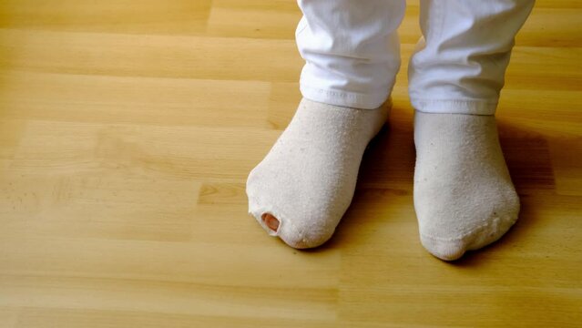close-up of female feet on the floor in gray light cotton socks with hole, the concept of women's health, an unpleasant event at a party, poverty, a sudden embarrassment