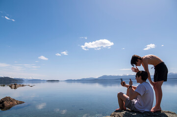 Hermanos utilizando el celular para una video llamada desde la costa del Lago Nahuel Huapi en Bariloche en sus vacaciones de verano. 