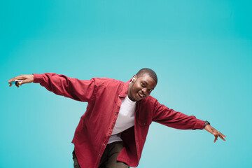 young African American man pictured isolated on gray background wearing casual clothes and hat dancing to music he is listening through wireless earphones, feeling relaxed and happy