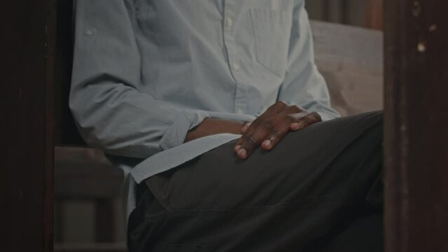 Cropped shot of unrecognizable Black man sitting on wooden bench in church and listening to sermon