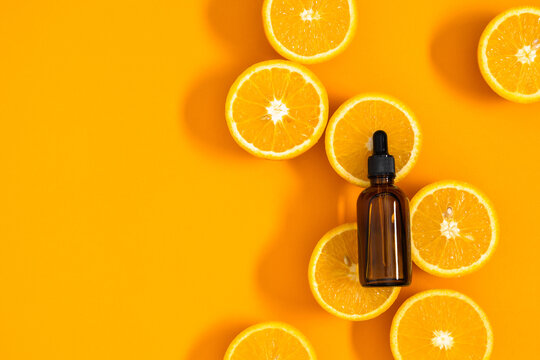 Natural orange essential oil in bottle and cut oranges fruit on  orange background table. Citrus oil for skin care, spa, massage, aromatherapy and natural medicine. Flat lay, top view, copy space