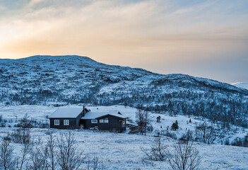 Traditional norwegen wooden house on a hill covered with snow in Eidfjord village during sunset, Norway