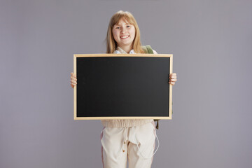 smiling teenager girl in beige tracksuit showing blank board