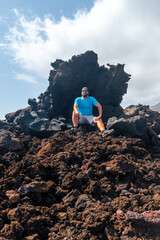 Young man sitting on the red stones on the volcanic trail in the village of Tamaduste on the coast of the island of El Hierro, Canary Islands, Spain