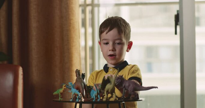 Little child playing with toys game at home. Cute preschool child talking with toys playing dinosaurs toys sit on table, happy kid explain paleontology having fun at home. Concept happy childhood. 