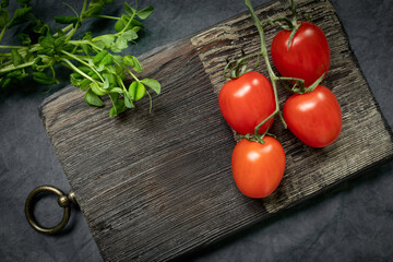 a branch with red ripe cherry tomatoes on a decorative kitchen board and bunch of micro greens. Farm organic products, diet, healthy food concept