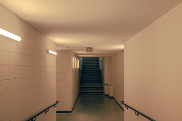 Interior view of an empty corridor and stairwell with concrete block walls, fluorescent light fixtures, teal and orange grading, nobody