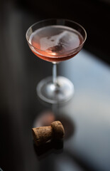 Glass of pink champagne and a cork on a glass table by a window at sunset
