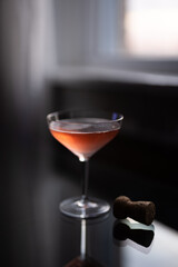 Glass of pink champagne and a cork  on a glass table by a window at sunset