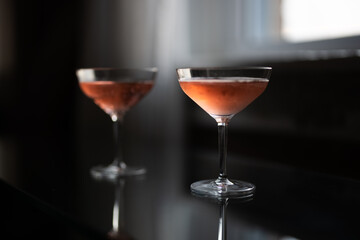 Two glasses of pink champagne on a glass table by a window at sunset