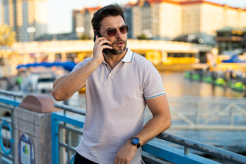 Portrait of handsome stylish man chatting on phone in big city. Sexy man in casual clothes talking on phone on the street. Successful male model in the urban lifestyle. Business phone conversation.