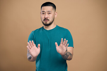 Serious asian man with beard making stop gesture showing palms of hands