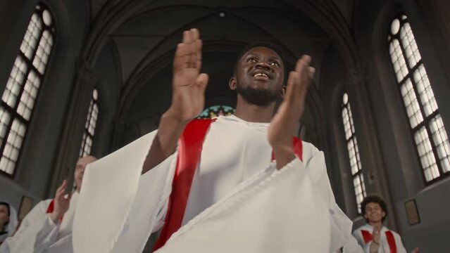 Low angle of young Black man with other choir members making performance in Catholic Church