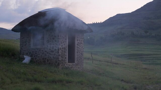 Cook fire smoke billows from small stone guard shack in Lesotho Africa
