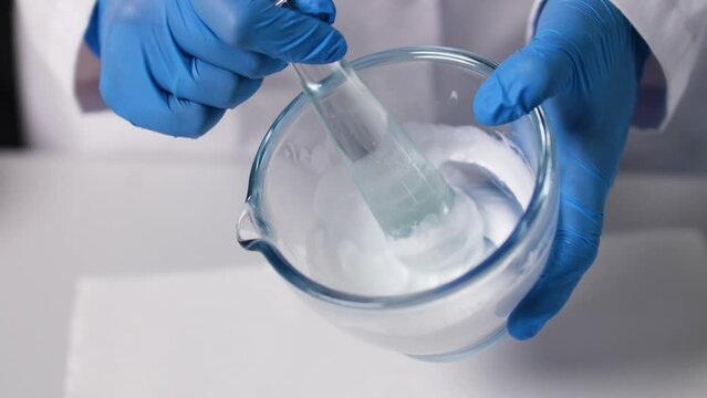 A cream is mixed in a glass bowl by stirring it. Macro and slow motion. Blue Gloves.