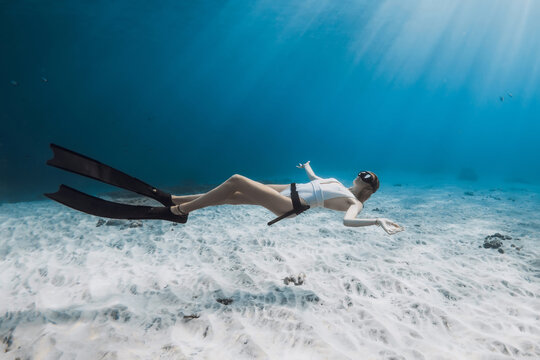 Freediver girl in white swimwear glides in tropical blue ocean
