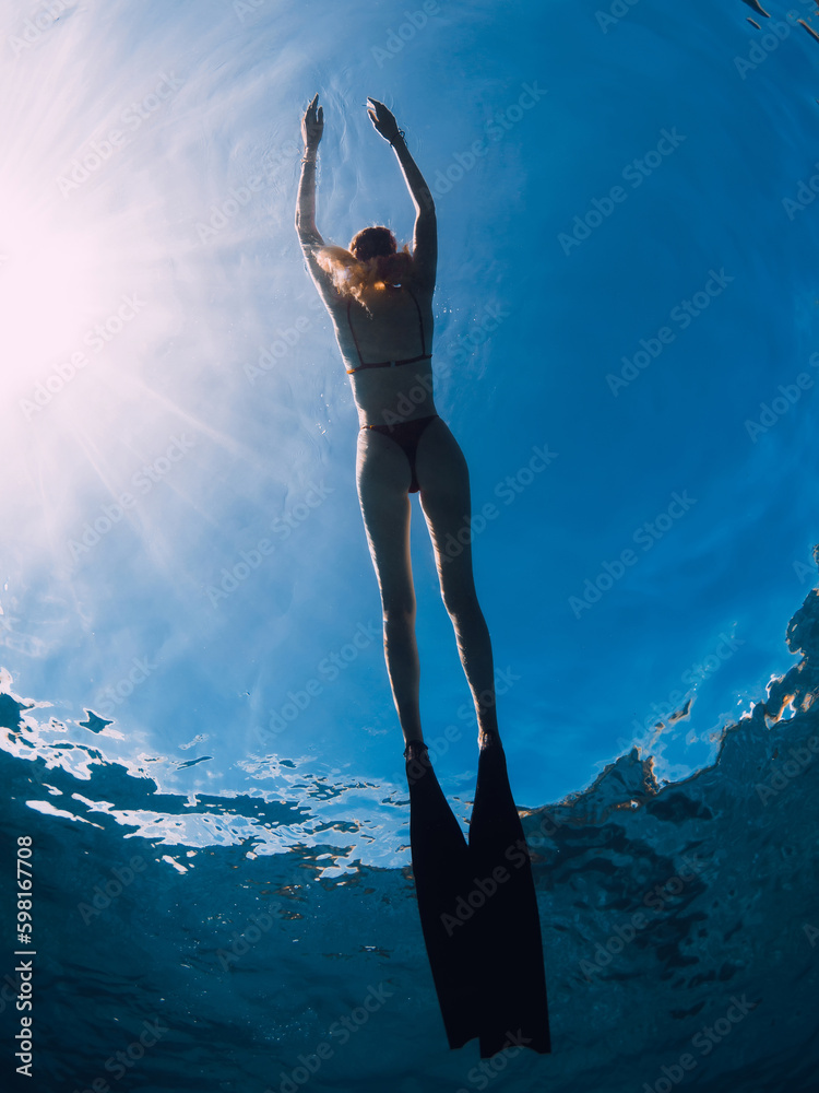 Wall mural Woman freediver relax with fins on the ocean surface. Freediving and sunlight in blue ocean