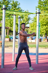 Young fit shirtless black man warming up in a calisthenics park outdoors on sunny day. Fitness and sport lifestyle.