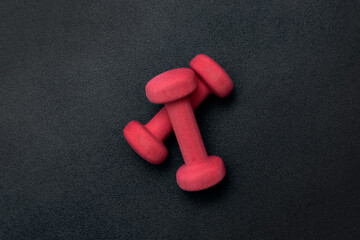 Two red dumbbells on a black background. View from above. Sport equipment.