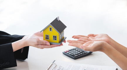 Female real estate agent and insurance salesman giving a sample house to a client after signing the sale at the office.