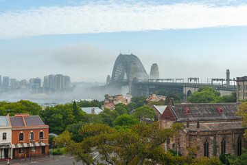 Strip of white cloud crosses sky over Sydney Harbour bridge and mist hangs over harbour and city in...