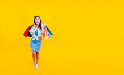 Pretty Asian woman in trendy summer fashion is smiling and holding shopping bag in happiness for discount sale isolated on yellow background for advertising and promotion event concept
