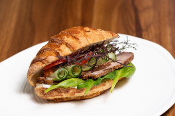 Croissant sandwich with meat and vegetables on a white plate, closeup, side view. Healthy breakfast concept, restaurant menu