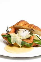 Croissant sandwich with cream cheese, salmon and arugula on a white plate, close-up. Isolated on white background. Healthy breakfast concept, restaurant menu