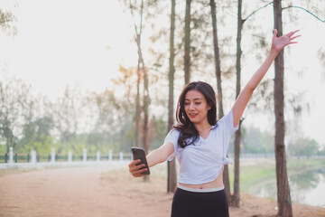 A beautiful female is using mobile phone to video calll or selfie while stretching in th early morning. Concept of city life or urban activity with technology. New normal life. Exercise and jogging
