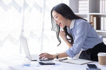 Portrait of Happy Excited young asian woman at workplace office desk, successful Asian female reading good news technology online, employee freelance finance concepts.