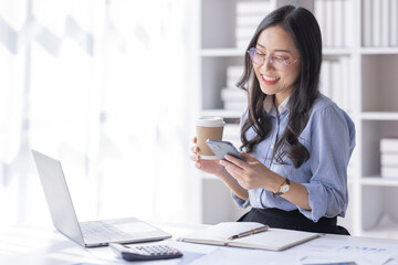 Business Asian woman hold phone and use laptop at the workplace. Project stats financial data sales charts on laptop and cellphone Asian finance concept
