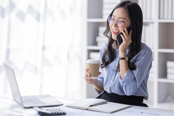 Obraz premium Cheerful business Asian woman freelancer making telephone call share good news about project working in office workplace, business finance concept. 