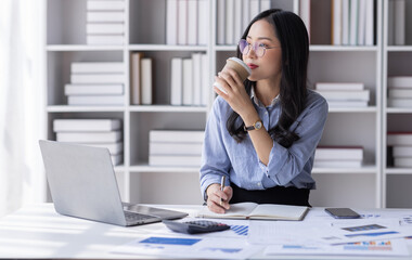 Asian Business woman using calculator and laptop for doing math finance on an office desk, tax, report, accounting, statistics, and analytical research concept
