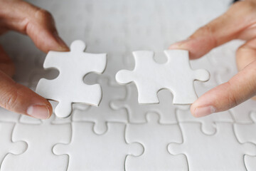 Business woman hand is trying to connect couple White jigsaw puzzle piece on a blue background. Symbol of association and connection. Concept of business strategy.