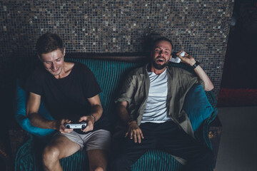 Two friends of handsome guys play a console at home, strong emotions, joy, annoyance, victory, laughter, surprise, computer games, joysticks