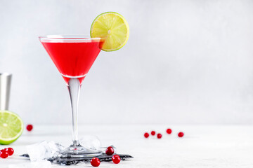 Cosmopolitan alcoholic cocktail drink with vodka, liqueur, cranberry juice, lime and ice. Gray table background, copy space