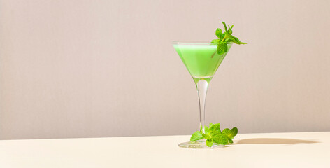 Grasshopper green alcoholic cocktail drink with mint liqueur, cream, ice and fresh mint. Beige background, hard light, shadow pattern, copy space