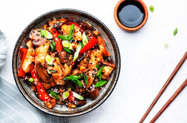 Stir fry chicken fillet, red paprika, mushrooms, green chives and sesame seeds in ceramic bowl Asian cuisine dish. White kitchen table background, top view