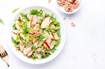 Waldorf salad with red and green apple, celery, lettuce, chicken fillet, arugula and walnuts on plate, white table background, top view