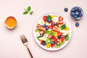 Summer healthy fruit and berry salad with strawberries, blueberries, banana, kiwi, orange and mint leaves, pink background, top view
