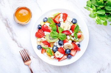 Summer fruit and berry salad with cottage cheese and mint leaves with honey dressing, marble table background, top view
