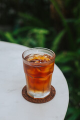 Lemon cool iced tea in summer. A drink with fruit on a round white table against the background of palm trees. Stylish cold drink concept with space for text