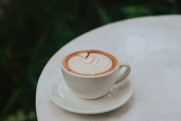 Mokachino with chocolate and beautiful foam in a white cup on a round table. Aromatic coffee with cocoa on the background of plants. Stylish concept for advertising coffee and cafe