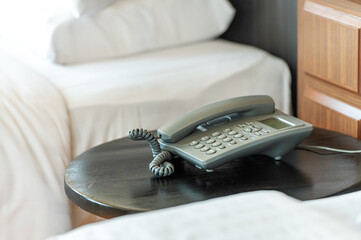 Fototapeta premium Hotel phone services concept.Closeup of hotel white telephone phone type keypad button phone number cable wire in bed room.Vintage old telephone is a keypad handset.